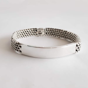 Puede incluir: Una pulsera de plata con un diseño de eslabones de cadena y una etiqueta rectangular plana. La etiqueta está en blanco y se puede grabar.