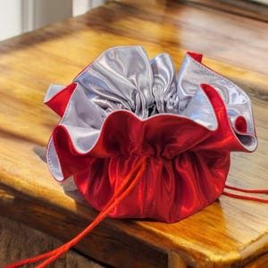 Op de afbeelding: Een rood satijnen trekkoordzakje met een zilveren voering. Het zakje is open en het trekkoord is zichtbaar.