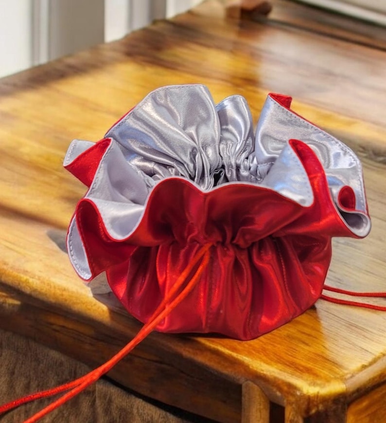 Op de afbeelding: Een rood satijnen trekkoordzakje met een zilveren voering. Het zakje is open en het trekkoord is zichtbaar.