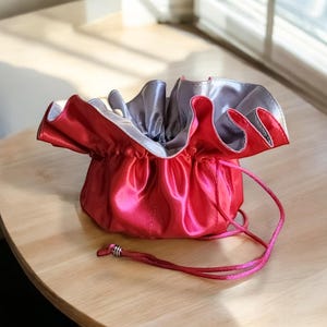 Op de afbeelding: Een roze satijnen trekkoordtasje met een zilveren voering. Het tasje is open en het trekkoord is zichtbaar.