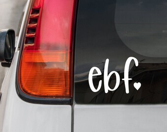 May include: White vinyl sticker with the text "ebf." and a small heart next to it, applied to the back window of a silver car.