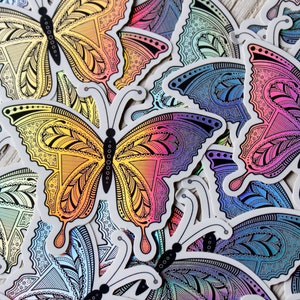 May include: A collection of colorful butterfly stickers with intricate patterns. The stickers feature a gradient of colors, including yellow, orange, pink, purple, and blue. The butterfly designs have detailed wing patterns and black antennae.