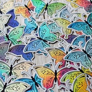 May include: A collection of colorful butterfly stickers with intricate patterns. The stickers feature a variety of colors, including blue, green, yellow, and purple, with a metallic sheen. The butterflies have detailed wing designs and are arranged on a light-colored surface.