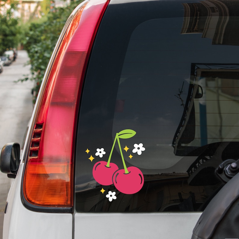 May include: A car window decal with two red cherries and white flowers. The cherries have green stems and leaves.