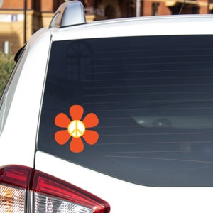 May include: A white car with a peace sign sticker on the back window. The sticker is a red flower with a yellow peace sign in the center.