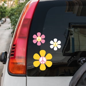 May include: Three peace sign stickers in the shape of flowers. The flowers are yellow, pink, and white. The peace signs are white.