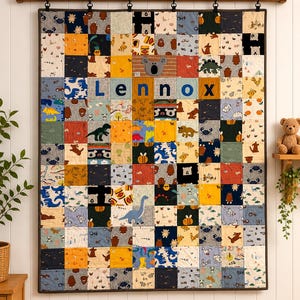 May include: A rectangular patchwork quilt featuring a grid of colourful fabric squares with various animal and nature prints. The name Lennox is printed in large blue letters across the centre, accompanied by a grey koala face appliqué.