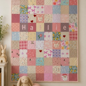 May include: A patchwork quilt featuring a grid of various fabric squares in shades of pink, blue, and white. The quilt displays the name Hallie in white letters across the centre, accented with embroidered bunny faces, red hearts, and floral patterns.