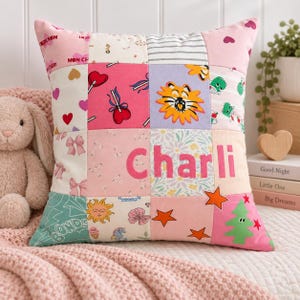 May include: A square patchwork cushion featuring various fabric squares with pink, white, and multi-coloured patterns including hearts, lollipops, a lion, stars, and a Christmas tree. The name Charli is appliqued in pink letters across the centre.