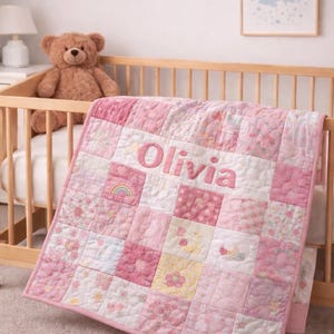 May include: A pink and white patchwork baby quilt, embroidered with the name "Olivia", draped over a wooden cot. A brown teddy bear sits inside the cot. The quilt features floral and rainbow patterns.