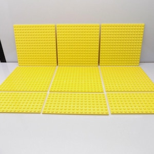 May include: A collection of nine square yellow plastic building block baseplates arranged in a grid pattern. Each baseplate features a uniform surface of raised circular studs designed for connecting interlocking construction bricks.