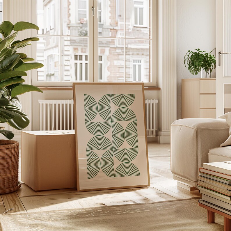 May include: A framed print with a geometric design of green concentric circles on a white background. The print is leaning against a cardboard box in a room with a large window and a white couch.
