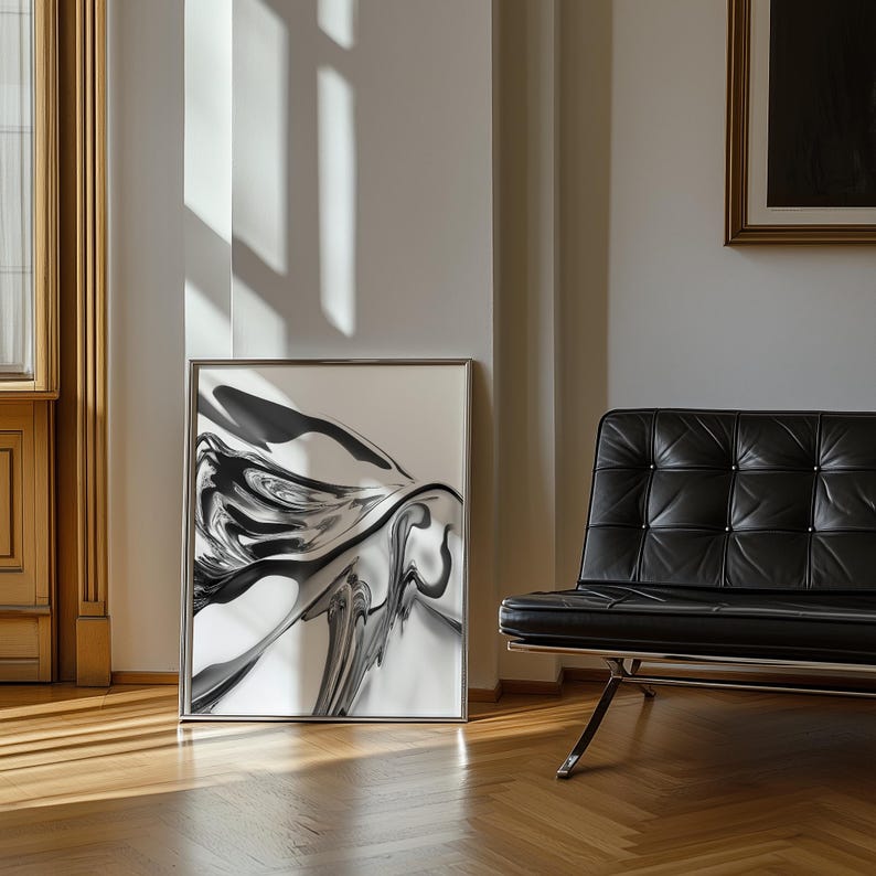 Pode incluir: Uma impress&atilde;o de arte abstrata emoldurada com uma moldura prateada. A obra de arte apresenta um design em preto e branco. A impress&atilde;o est&aacute; encostada a uma parede branca, com uma cadeira de couro preta e ch&atilde;o de madeira no fundo.