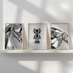 Pode incluir: Tr&ecirc;s impress&otilde;es de arte emolduradas em uma prateleira branca. Duas impress&otilde;es apresentam designs prateados abstratos e reflexivos. A impress&atilde;o central mostra uma estatueta prateada. Todas as molduras t&ecirc;m bordas de madeira clara.