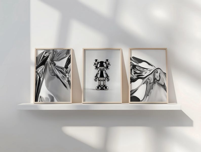 Pode incluir: Tr&ecirc;s impress&otilde;es de arte emolduradas em uma prateleira branca. Duas impress&otilde;es apresentam designs prateados abstratos e reflexivos. A impress&atilde;o central mostra uma estatueta prateada. Todas as molduras t&ecirc;m bordas de madeira clara.