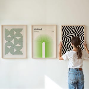 May include: Three framed prints on a white wall. The print on the left features a geometric pattern of green semi-circles. The middle print features a green and white gradient arch with the text "BAUHAUS Ausstellung 1923". The print on the right features a black and white optical illusion pattern.