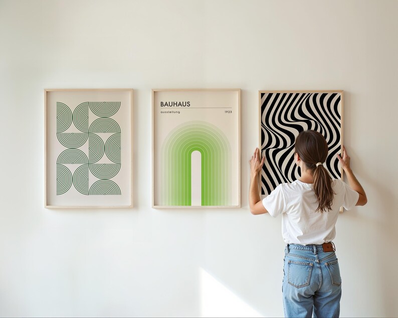 May include: Three framed prints on a white wall. The print on the left features a geometric pattern of green semi-circles. The middle print features a green and white gradient arch with the text "BAUHAUS Ausstellung 1923". The print on the right features a black and white optical illusion pattern.