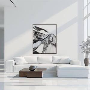 Pode incluir: Impress&atilde;o de arte abstrata em preto e branco em uma moldura preta. A obra de arte apresenta formas girat&oacute;rias e l&iacute;quidas. A impress&atilde;o est&aacute; pendurada acima de um sof&aacute; seccional branco em uma sala de estar moderna. Uma mesa de centro marrom escuro e um vaso decorativo est&atilde;o em frente ao sof&aacute;.