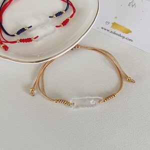 May include: A collection of handmade bracelets. The bracelets feature red, navy blue, and gold cord with gold-colored beads. One bracelet has a clear rectangular charm with a floral design. The website www.zoleeshop.com is visible.