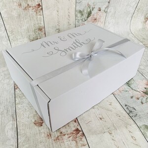 May include: A white gift box with a silver ribbon and the text "Mr & Mrs Smith" in a cursive font.
