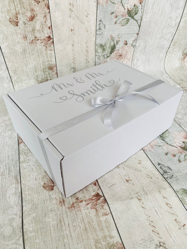 May include: A white gift box with a silver ribbon and the text "Mr & Mrs Smith" in a cursive font.