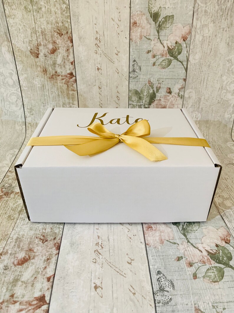 May include: White gift box with a gold ribbon and the name "Kate" written on the top.