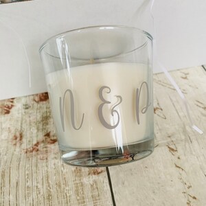 May include: A clear glass candle jar with a white candle inside. The candle has the letters "N & D" printed on the side in gray.