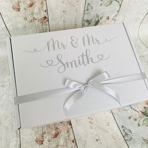 May include: White gift box with a silver ribbon and the text "Mr & Mrs Smith" in a cursive font.