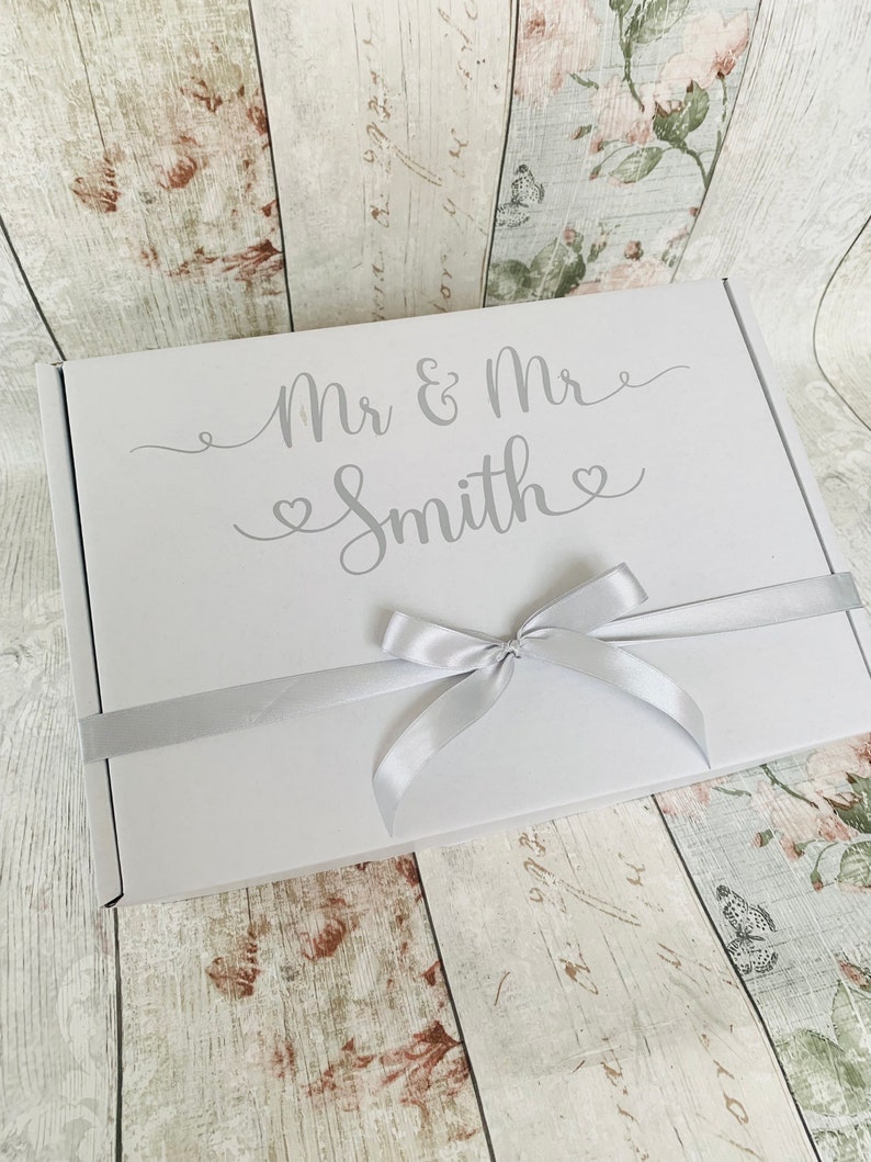 May include: White gift box with a silver ribbon and the text "Mr & Mrs Smith" in a cursive font.