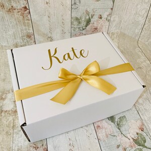 May include: A white gift box with a gold ribbon and bow. The box is personalized with the name "Kate" in gold lettering.