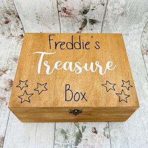 May include: A wooden treasure box with a hinged lid and a brass latch. The box is stained a light brown colour and has the words "Freddie's Treasure Box" written on the top in black and white lettering. There are five black stars around the text.