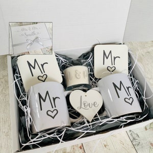 May include: A white gift box filled with a white candle, two white mugs, two white coasters, and a white wooden heart. The mugs, coasters, and heart all have the word "Mr" written on them with a small heart.