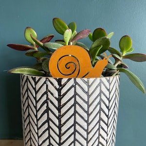 以下が含まれることがあります： 黒と白のヘリンボーン柄の鉢に植えられた多肉植物と、金属製のカタツムリの装飾