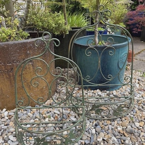 May include: Two sage green metal wall planters featuring an arched back with decorative scrollwork and a semi-circular basket base. The front of each basket is adorned with flat metal leaf cutouts, and the structure is made of thin wire.