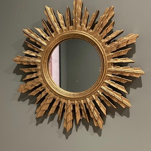 K&ouml;nnte beinhalten: Ein goldener Sonnenspiegel mit einer runden, reflektierenden Oberfl&auml;che. Der Spiegel hat einen dekorativen, verzierten Rahmen mit einem Sonnenstrahlendesign.