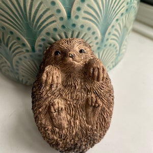 K&ouml;nnte beinhalten: Eine kleine, braune, keramische Igelfigur, die sich zusammengerollt hat. Die Figur hat eine detaillierte, strukturierte Oberfl&auml;che, die Fell &auml;hnelt.