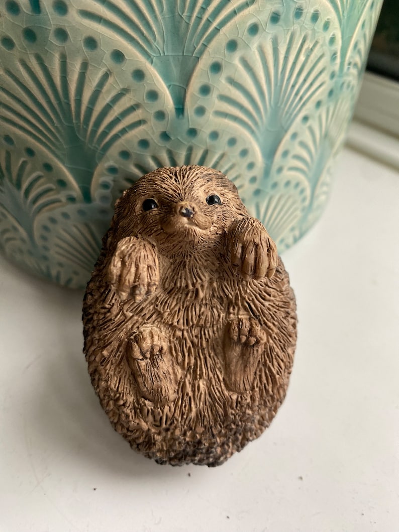 K&ouml;nnte beinhalten: Eine kleine, braune, keramische Igelfigur, die sich zusammengerollt hat. Die Figur hat eine detaillierte, strukturierte Oberfl&auml;che, die Fell &auml;hnelt.