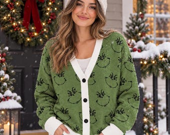 May include: A green V-neck button-down cardigan featuring a repeating black outline print of a character face. The knit sweater has a white trim along the button placket, cuffs, and hem, and is worn with a white top and blue denim jeans.