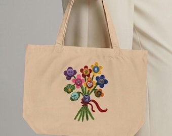 May include: A beige canvas tote bag featuring an embroidered bouquet of colorful flowers. Each flower center contains small circular text in various colors including purple, pink, green, red, yellow, and blue, tied together with a red ribbon.