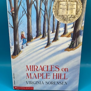 May include: A book cover featuring a snowy forest scene with a girl walking through the trees. The book title is "Miracles on Maple Hill" by Virginia Sorensen. The cover also displays a John Newbery Medal award.