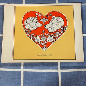 May include: A vintage book cover with a red heart design featuring two white bears facing each other. The heart is surrounded by white flowers and vines. The text "Weekly Reader Books" is printed at the bottom of the cover.