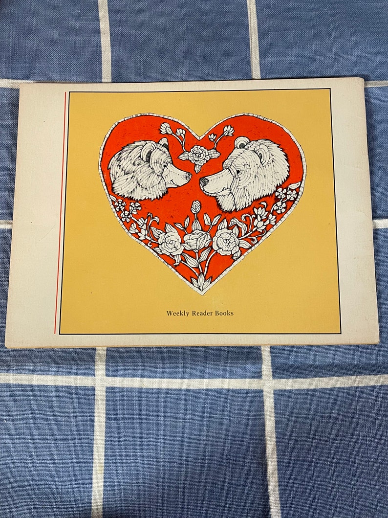 May include: A vintage book cover with a red heart design featuring two white bears facing each other. The heart is surrounded by white flowers and vines. The text "Weekly Reader Books" is printed at the bottom of the cover.