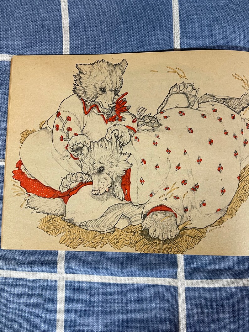 May include: Two white bears wearing red and white patterned dresses are lying on a bed of straw. The bear on the left is sitting up and looking at the bear on the right.