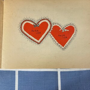 May include: Two red hearts with lace trim and black ribbon bows. The hearts are on a cream-colored page with the text "For E.B. -E.B." and "For J.H. -J.B."