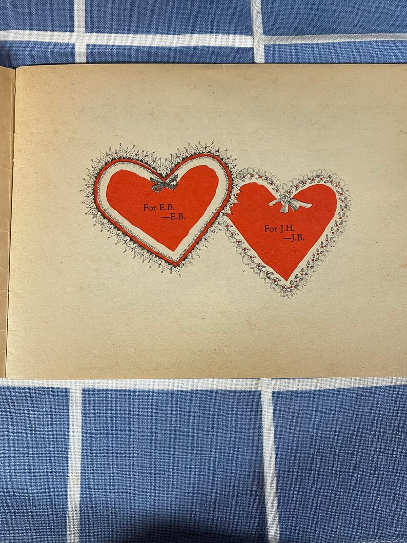 May include: Two red hearts with lace trim and black ribbon bows. The hearts are on a cream-colored page with the text "For E.B. -E.B." and "For J.H. -J.B."