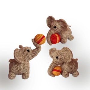May include: Three crocheted gray elephant toys are playing with orange and red balls. The elephants are sitting on a white background.
