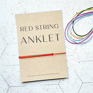 May include: Red string anklet on a brown card with the text "RED STRING ANKLET" and the website address "www.etsy.com/uk/shop/DaisyJewelleryGifts".