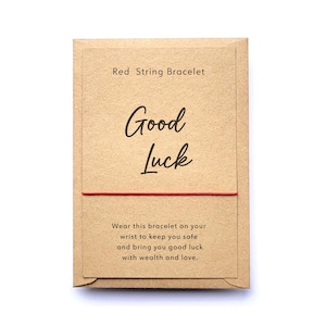 May include: A red string bracelet packaged in a brown paper envelope with the text "Red String Bracelet", "Good Luck", and "Wear this bracelet on your wrist to keep you safe and bring you good luck with wealth and love."