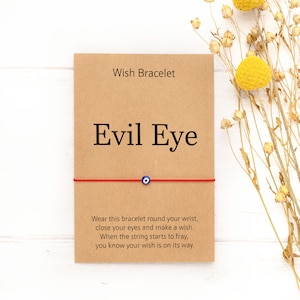 May include: Red string bracelet with a blue evil eye charm. The card reads "Wish Bracelet Evil Eye" and includes instructions on how to make a wish.