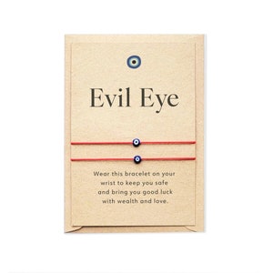 May include: Two red string bracelets with blue evil eye charms. The card reads "Evil Eye" and "Wear this bracelet on your wrist to keep you safe and bring you good luck with wealth and love."